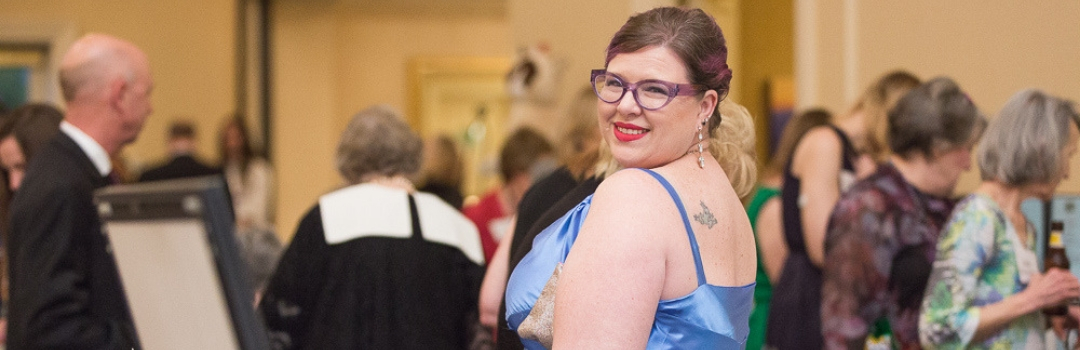 Tuxedo Cat Ball Attendee With Purple Cat Eye Glasses and Blue Dress Looking At Camera Over Her Shoulder